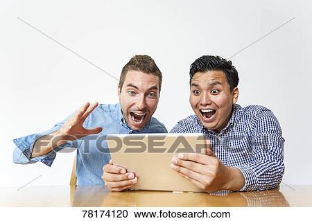 Stock Image - International friends enjoying content on a tablet. Fotosearch