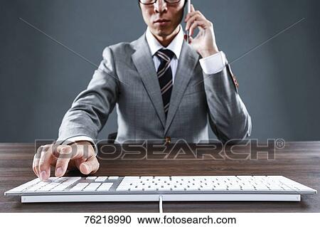 Stock Image - Japanese businessman working at desk. Fotosearch