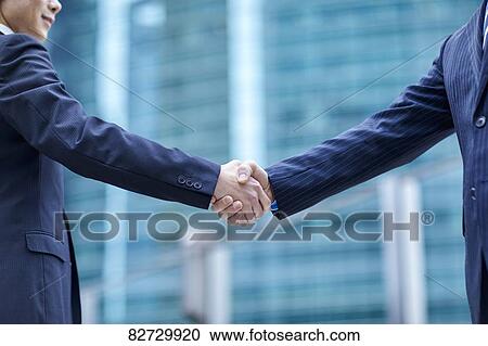 Stock Image - Japanese businesspeople shaking hands downtown Tokyo. Fotosearch