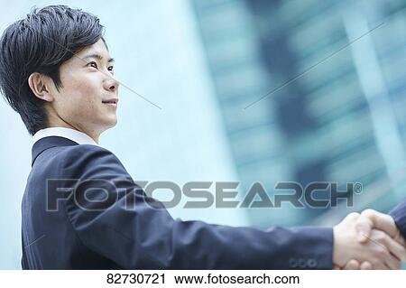 Stock Image - Japanese businesspeople shaking hands downtown Tokyo. Fotosearch