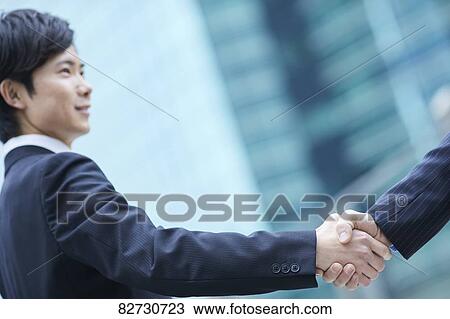 Stock Image - Japanese businesspeople shaking hands downtown Tokyo. Fotosearch