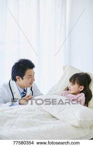Picture - Japanese doctor with a patient in bed. Fotosearch
