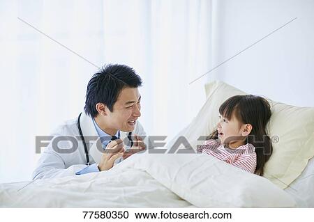 Stock Image - Japanese doctor with a patient in bed. Fotosearch