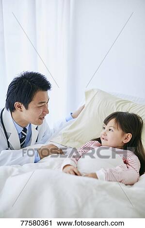Stock Image - Japanese doctor with a patient in bed. Fotosearch