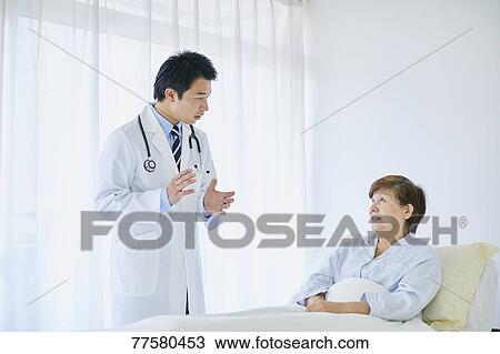 Stock Image - Japanese doctor with a patient in bed. Fotosearch