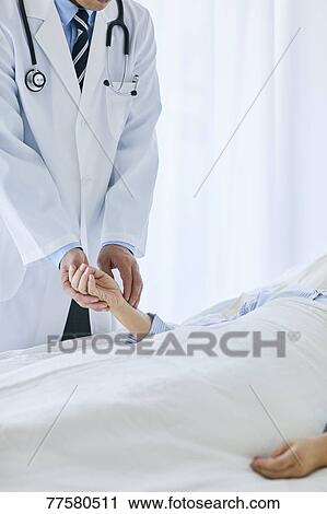 Stock Image - Japanese doctor with a patient in bed. Fotosearch