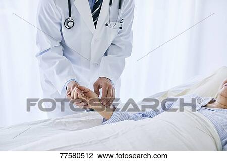 Stock Image - Japanese doctor with a patient in bed. Fotosearch