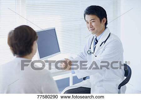 Stock Image - Japanese doctor with a patient in his studio. Fotosearch
