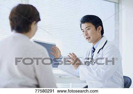 Stock Image - Japanese doctor with a patient in his studio. Fotosearch
