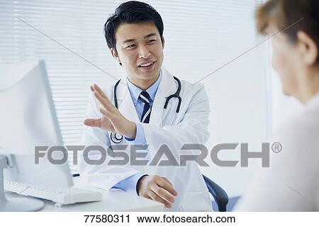 Stock Image - Japanese doctor with a patient in his studio. Fotosearch