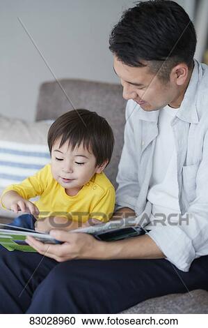 Stock Image - Japanese father and kid reading on the sofa. Fotosearch