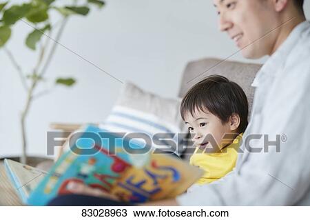 Stock Image - Japanese father and kid reading on the sofa. Fotosearch