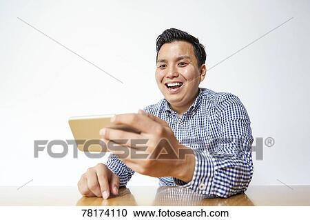 Stock Image - Japanese man enjoying content on a smartphone. Fotosearch