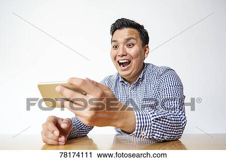 Stock Image - Japanese man enjoying content on a smartphone. Fotosearch