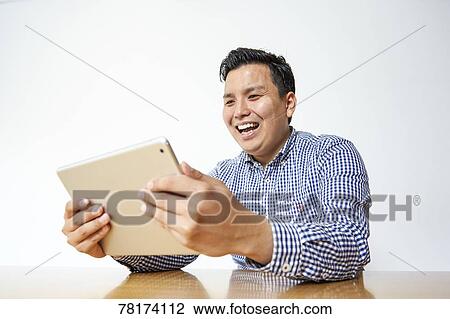 Japanese man enjoying content on a tablet View Large Photo Image Stock Image - Japanese man enjoying content on a tablet. Fotosearch