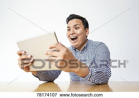 Japanese man enjoying content on a tablet View Large Photo Image Stock Photo - Japanese man enjoying content on a tablet. Fotosearch