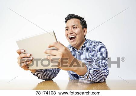 Japanese man enjoying content on a tablet View Large Photo Image Stock Photo - Japanese man enjoying content on a tablet. Fotosearch