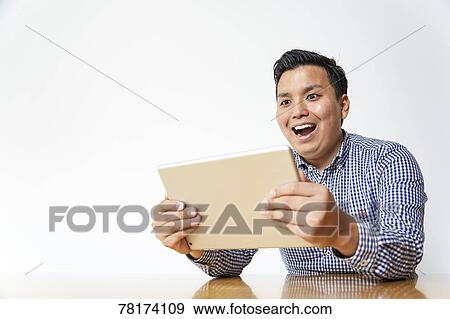 Stock Photo - Japanese man enjoying content on a tablet. Fotosearch