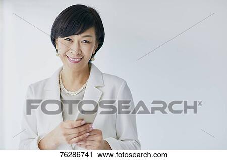 Stock Image - Japanese senior businesswoman against white wall. Fotosearch