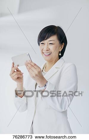 Stock Image - Japanese senior businesswoman against white wall. Fotosearch