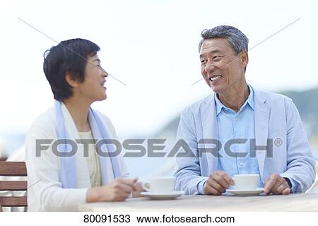 Stock Image - Japanese senior couple having a drink by the sea. Fotosearch