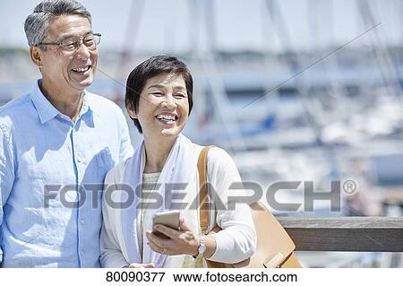 Stock Photo - Japanese senior couple having fun by the sea. Fotosearch