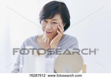 Stock Image - Japanese senior woman doing skin care. Fotosearch