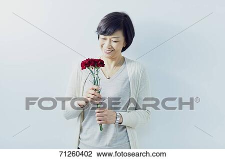 Stock Image - Japanese senior woman holding red roses. Fotosearch