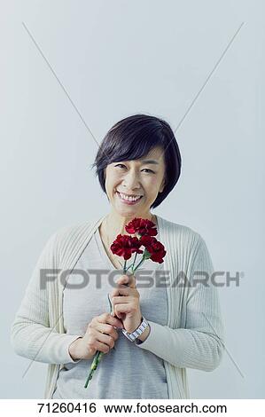 Stock Photograph - Japanese senior woman holding red roses. Fotosearch