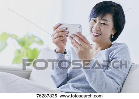 Stock Photography - Japanese senior woman on sofa. Fotosearch