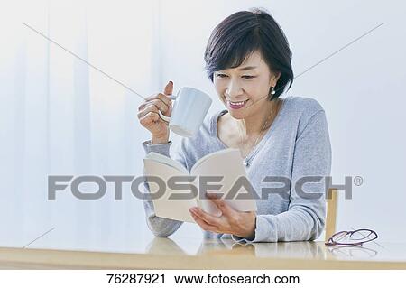 Stock Image - Japanese senior woman reading book at table. Fotosearch