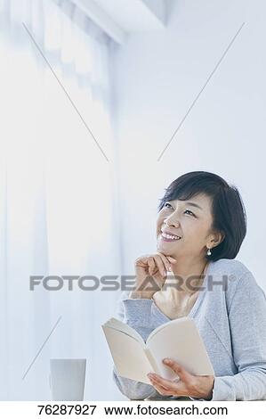 Stock Photo - Japanese senior woman reading book at table. Fotosearch