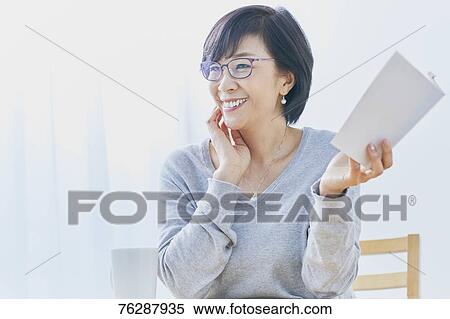 Stock Photography - Japanese senior woman reading book at table. Fotosearch
