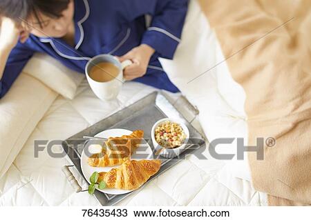 Stock Image - Japanese woman having breakfast in bed. Fotosearch
