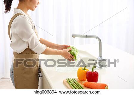 Picture - Japanese woman washing vegetables in the kitchen. Fotosearch