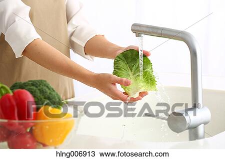 Stock Image - Japanese woman washing vegetables in the kitchen. Fotosearch