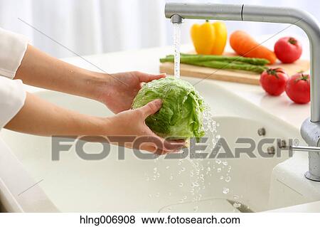 Stock Photo - Japanese woman washing vegetables in the kitchen. Fotosearch