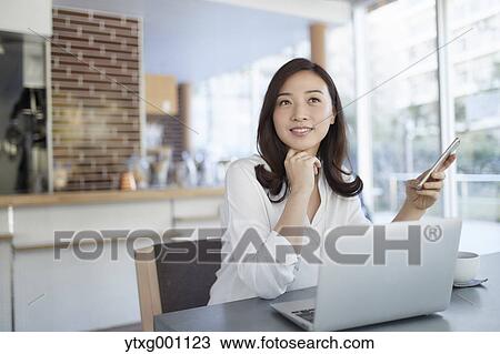 Stock Image - Japanese woman with smartphone in a stylish cafe. Fotosearch