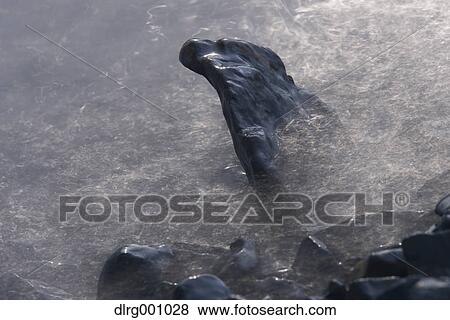 Stock Photo - Long exposure of black rocks in the water. Fotosearch