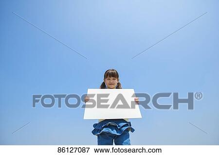 Stock Photo - Young Japanese girl holding whiteboard and blue sky. Fotosearch
