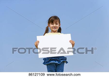 Stock Photo - Young Japanese girl holding whiteboard and blue sky. Fotosearch
