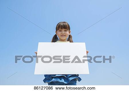 Stock Photograph - Young Japanese girl holding whiteboard and blue sky. Fotosearch