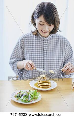 Stock Image - Young Japanese woman eating pancakes. Fotosearch
