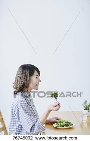 Stock Image - Young Japanese woman eating salad. Fotosearch