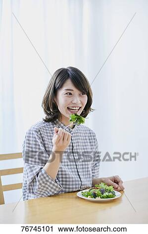 Stock Image - Young Japanese woman eating salad. Fotosearch