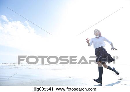 Stock Image - Young Japanese woman in a high school uniform running by the sea, Chiba, Japan. Fotosearch