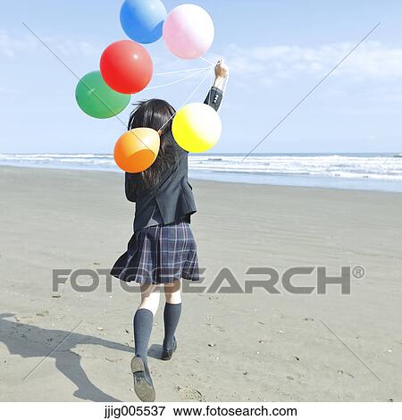 Stock Photo - Young Japanese woman in a high school uniform running with balloons by the sea, Chiba, Japan. Fotosearch