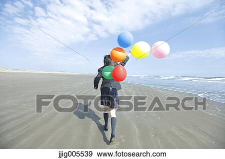 Stock Photo - Young Japanese woman in a high school uniform running with balloons by the sea, Chiba, Japan. Fotosearch