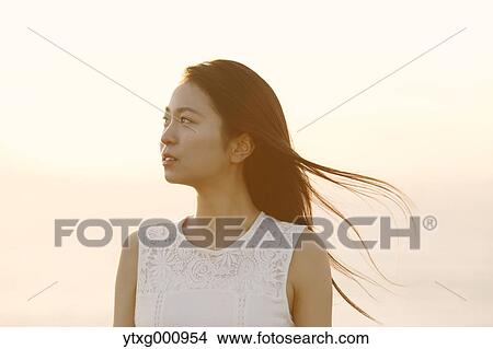 Picture - Young Japanese woman in a white dress at a cliff over the sea at sunrise, Chiba, Japan. Fotosearch
