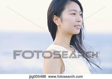 Stock Photograph - Young Japanese woman in a white dress at a cliff over the sea at sunrise, Chiba, Japan. Fotosearch